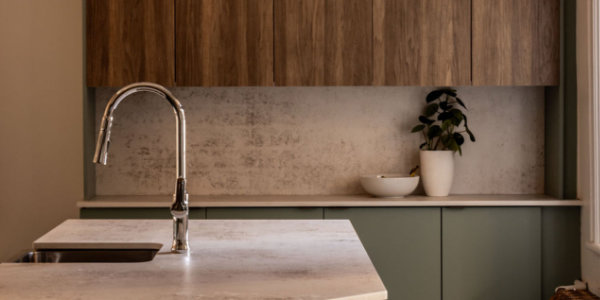 Une cuisine moderne au design minimaliste avec un comptoir en marbre et un robinet en métal élégant. Des armoires en bois avec une plante et un bol sur le comptoir.