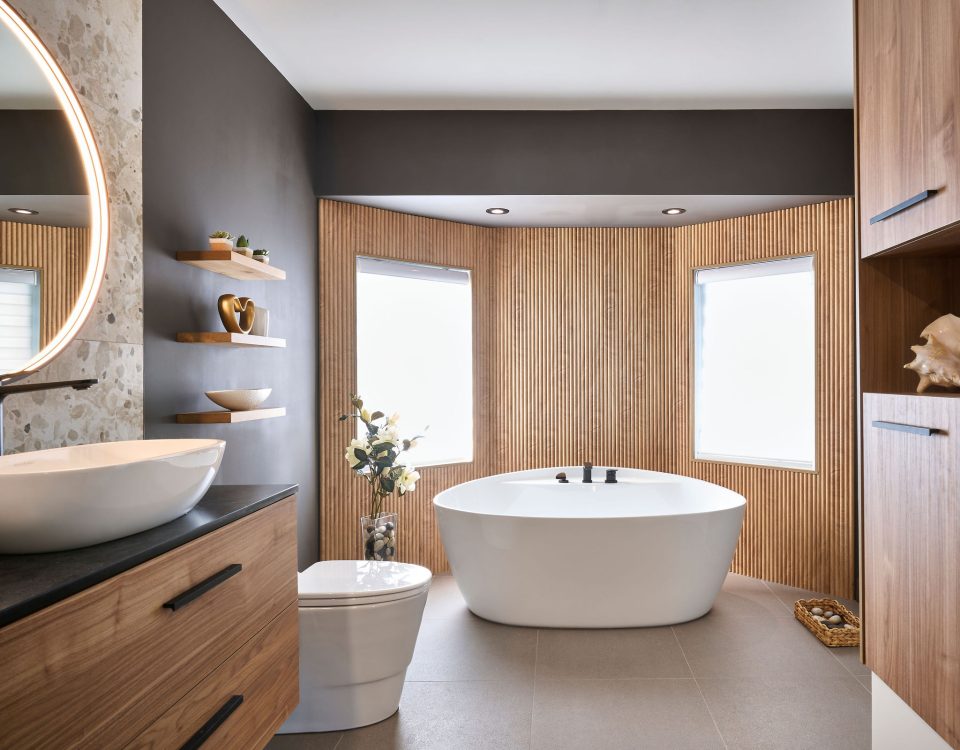 Salle de bain moderne rénovée à Montréal avec vanité en bois sur mesure, vasque contemporaine, baignoire îlot blanche et mur décoré de tasseaux en bois.