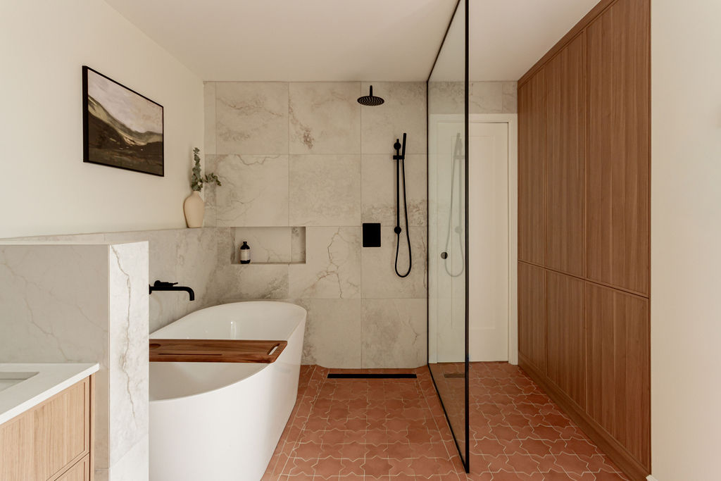Vue complète d’une salle de bain rénovée à Montréal avec baignoire îlot, douche à l’italienne, niches carrelées, muret intégré, sol en céramique terracotta et dressing sur mesure assorti à la vanité, projet réalisé par un entrepreneur général et designers d’intérieur.