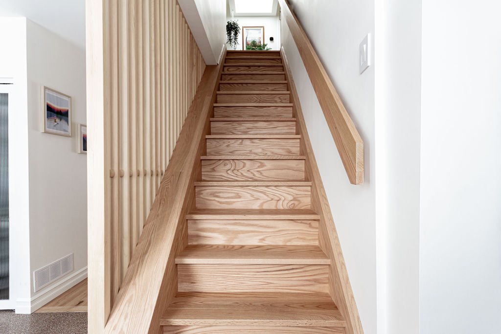 Escalier central avec main courante et tasseaux de bois jouant avec la lumière dans un projet de rénovation à Montréal par un entrepreneur général et designers d’intérieur.