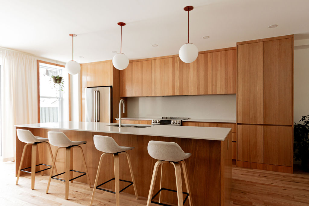 Cuisine sur mesure avec îlot central, armoires en mélaminé Finsa teinte chêne, comptoir et dosseret Desert Silver (Silestone), suspensions sphériques et quatre assises, projet réalisé par l’ébénisterie Crealux et un entrepreneur général à Montréal.