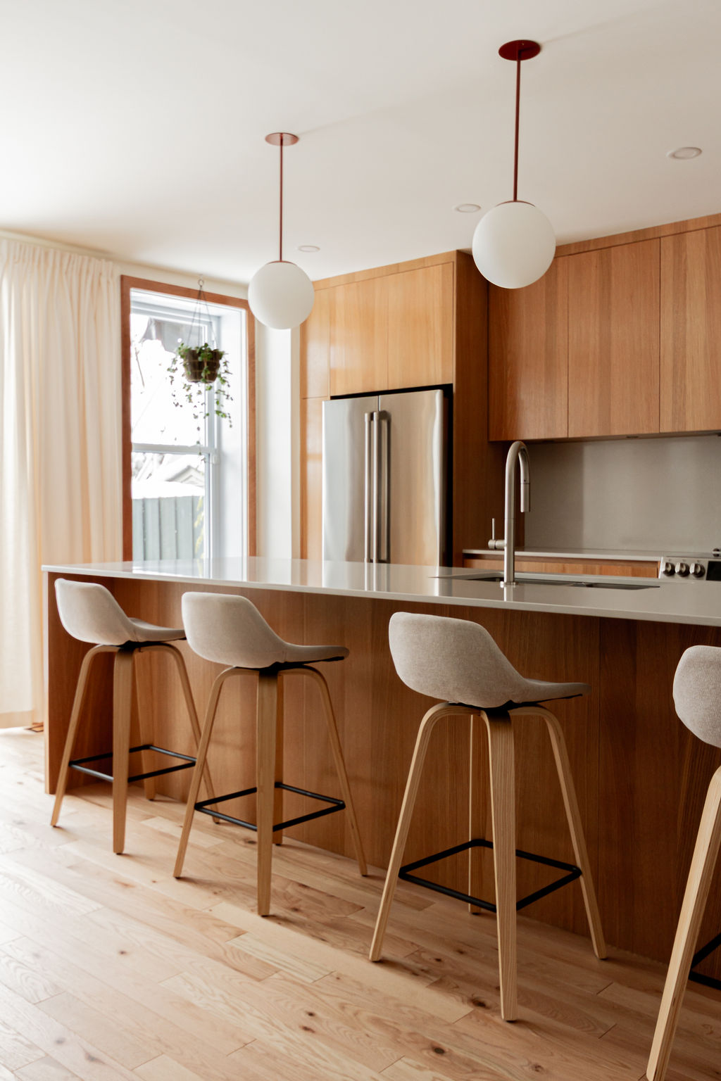 Cuisine sur mesure avec îlot central, armoires en mélaminé Finsa teinte chêne, comptoir et dosseret Desert Silver (Silestone), suspensions sphériques et quatre assises, projet réalisé par l’ébénisterie Crealux et un entrepreneur général à Montréal.