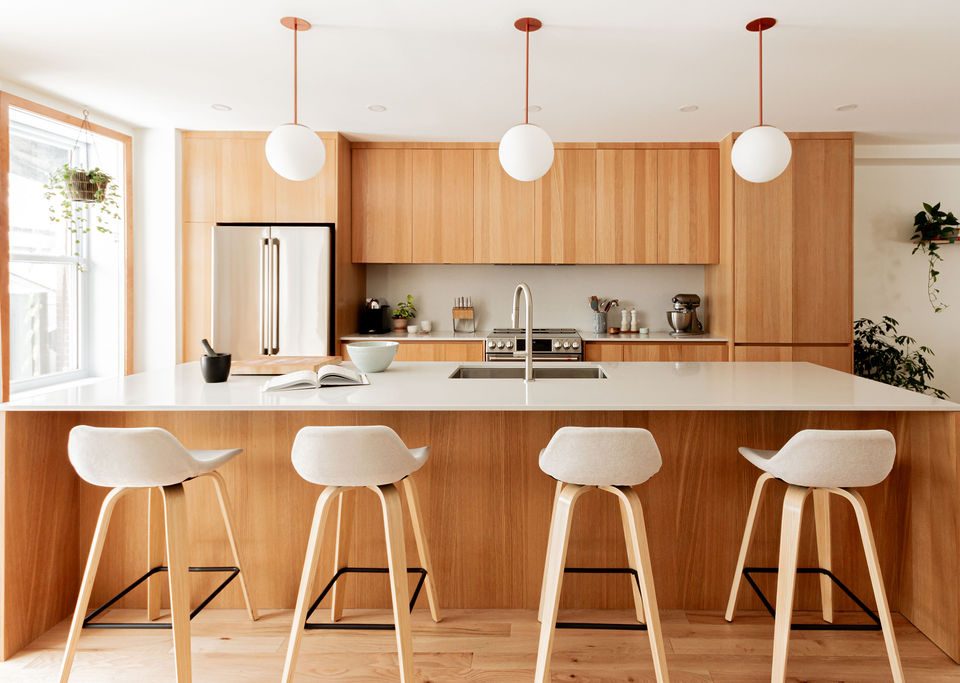 Cuisine sur mesure avec îlot central, armoires en mélaminé Finsa teinte chêne, comptoir et dosseret Desert Silver (Silestone), suspensions sphériques et quatre assises, projet réalisé par l’ébénisterie Crealux et un entrepreneur général à Montréal.