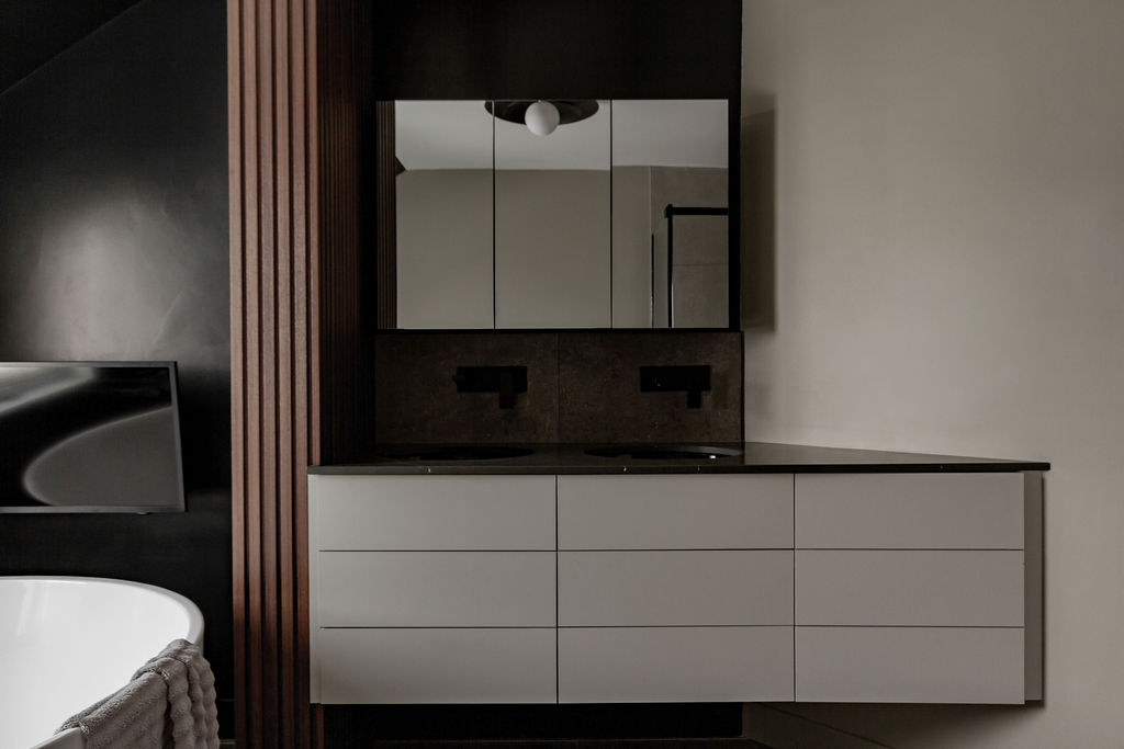 Vanité double suspendue sur mesure avec armoire à pharmacie miroir, robinetterie murale noir mat et colonne en lattes de bois dans une salle de bain moderne à Montréal.