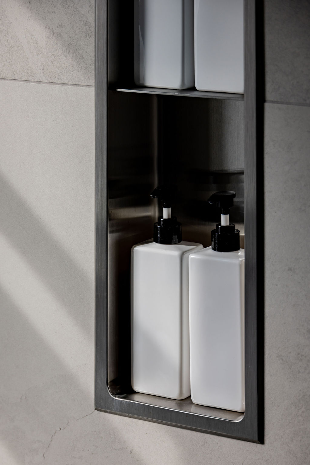 Gros plan sur une niche de douche encastrée en acier inoxydable brossé avec flacons de savon design, conçue par un designer d'intérieur à Montréal.