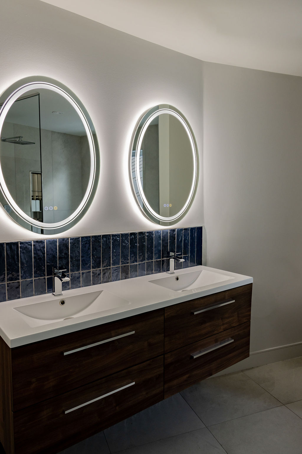 Vanité suspendue en bois avec double lavabo, dosseret en céramique bleu marin et deux miroirs ovales rétroéclairés LED, conçue par un designer d'intérieur à Montréal.