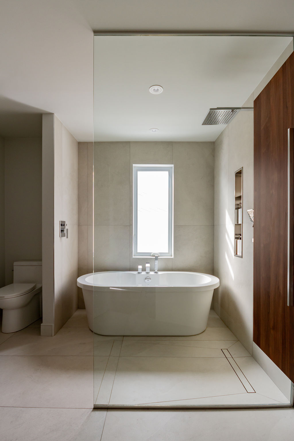 Salle de bain style spa à Montréal conçue par un designer d'intérieur, avec baignoire autoportante intégrée dans une douche italienne vitrée et grands carreaux de céramique beige.