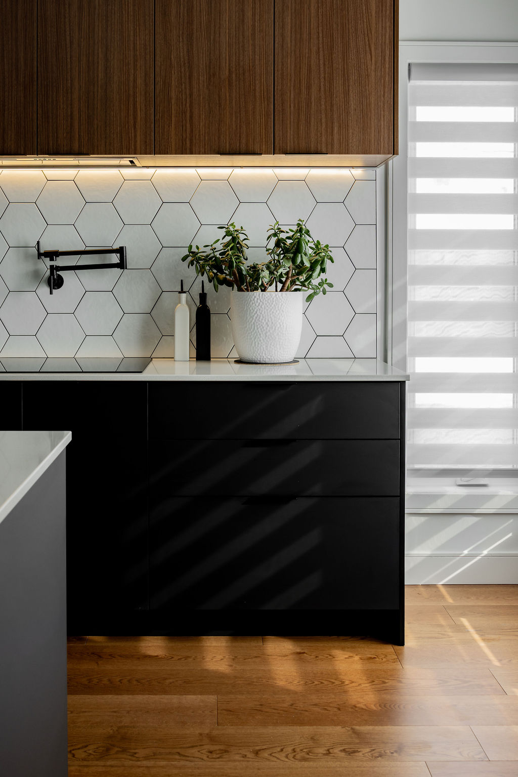 Cuisine bicolore à Montréal conçue par un designer d'intérieur, avec armoires basses noir mat, armoires hautes en bois, dosseret hexagonal blanc et remplisseur de casserole mural.