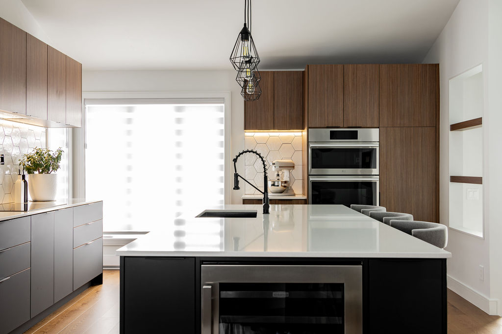Vue globale d'une cuisine contemporaine à Montréal conçue par un designer d'intérieur, avec grand îlot noir, comptoir en quartz blanc,cellier encastré et armoires en bois chaleureux.