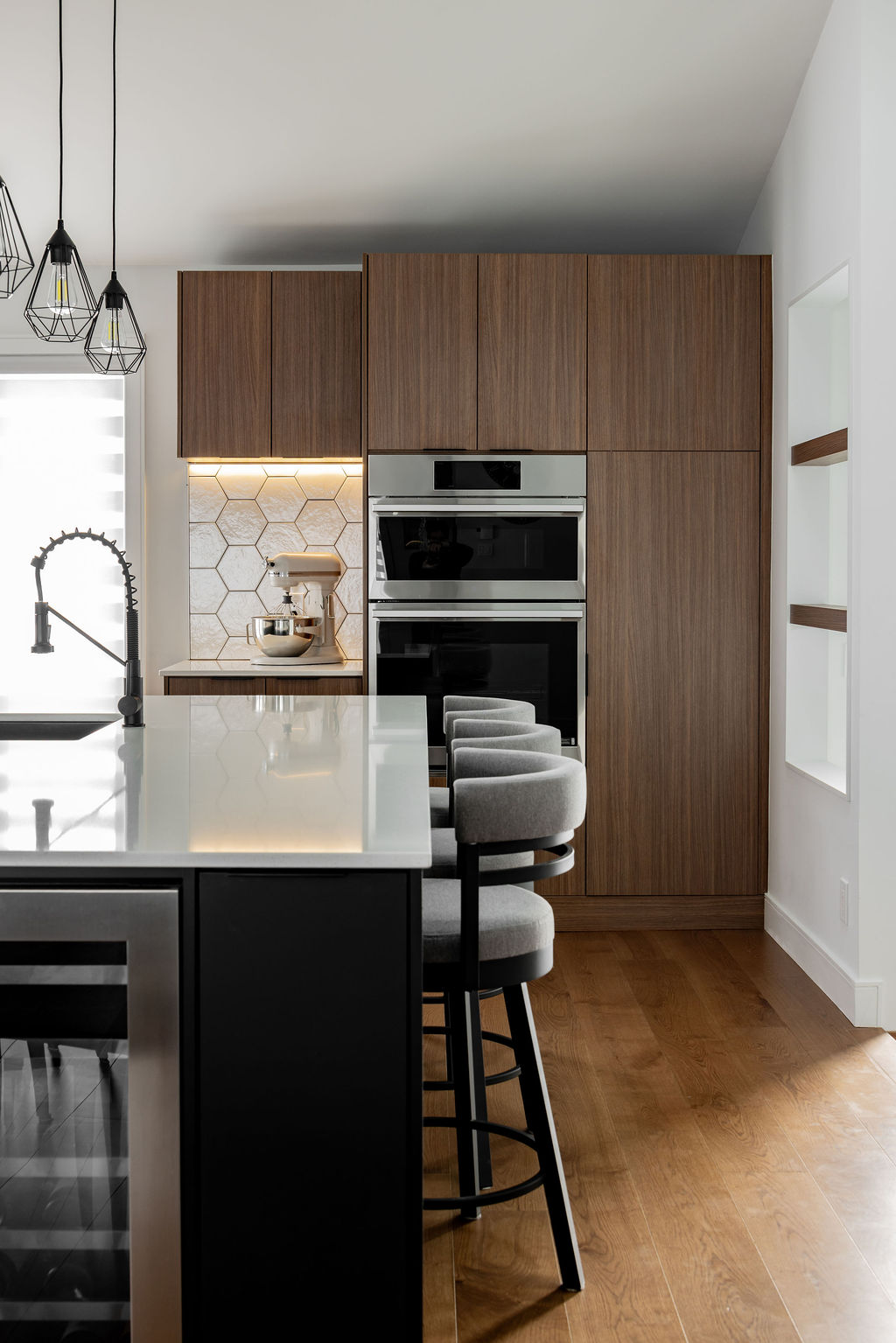 Îlot de cuisine noir avec tabourets de bar gris rembourrés, comptoir en quartz blanc, armoires en bois chaleureux et électroménagers encastrés à Montréal.