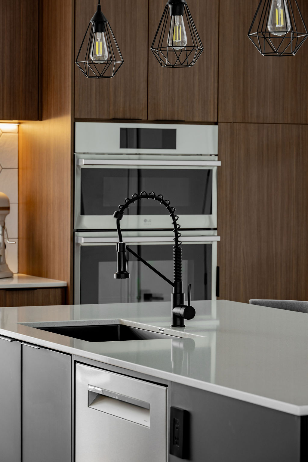 Évier sous-plan encastré dans un îlot de cuisine gris avec robinet col de cygne noir mat et suspensions géométriques, conçu par un designer d'intérieur à Montréal.