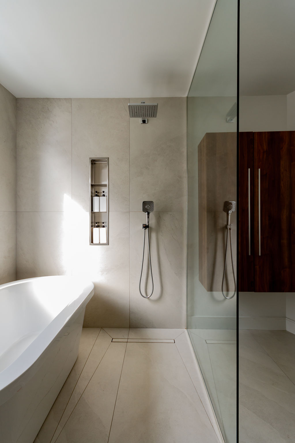Douche italienne avec pommeau de pluie, niche encastrée, drain linéaire et baignoire autoportante, conçue par un designer d'intérieur à Montréal.