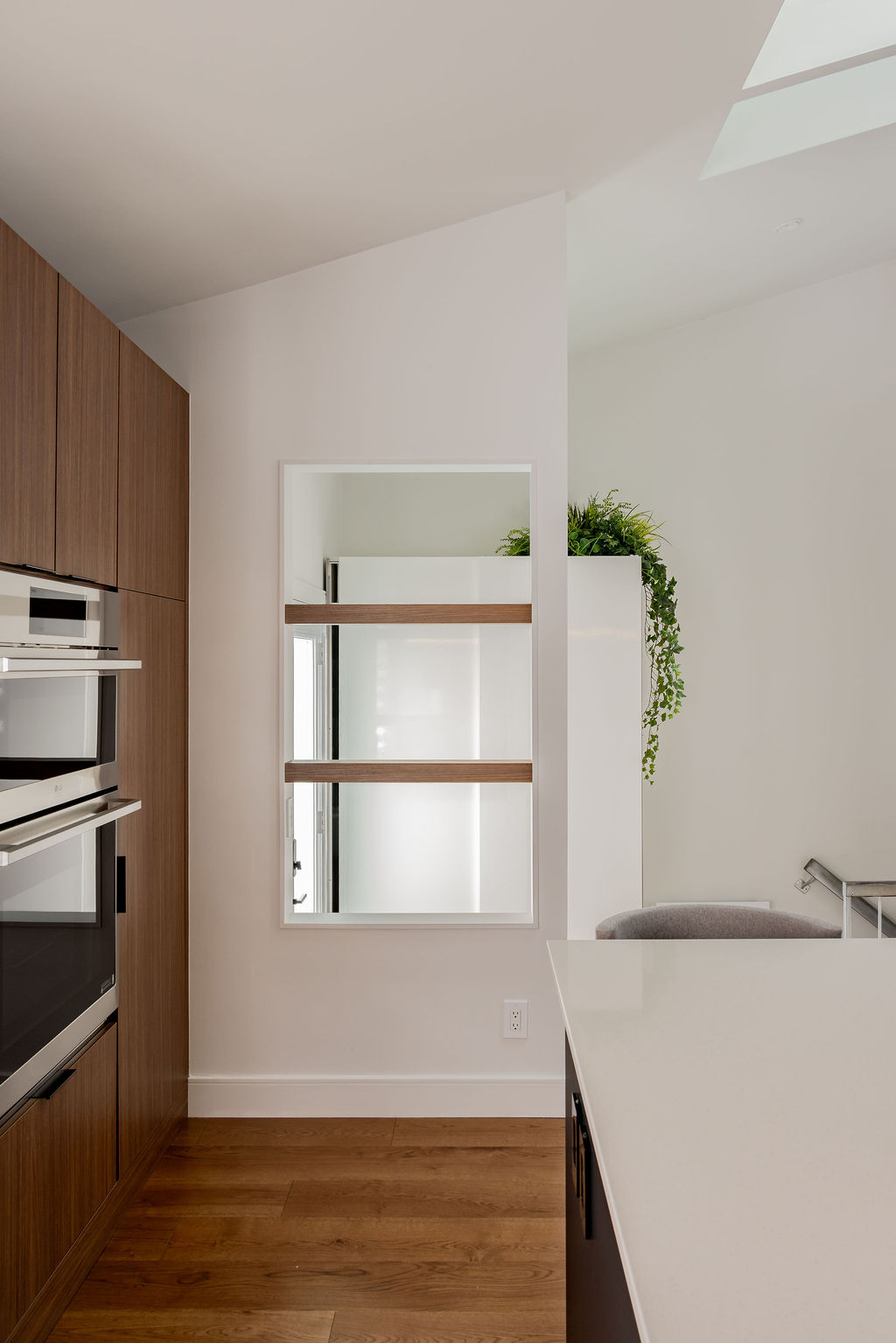 Ouverture architecturale murale avec étagères en bois intégrées dans une cuisine moderne à Montréal, créée par un designer d'intérieur pour maximiser la lumière.