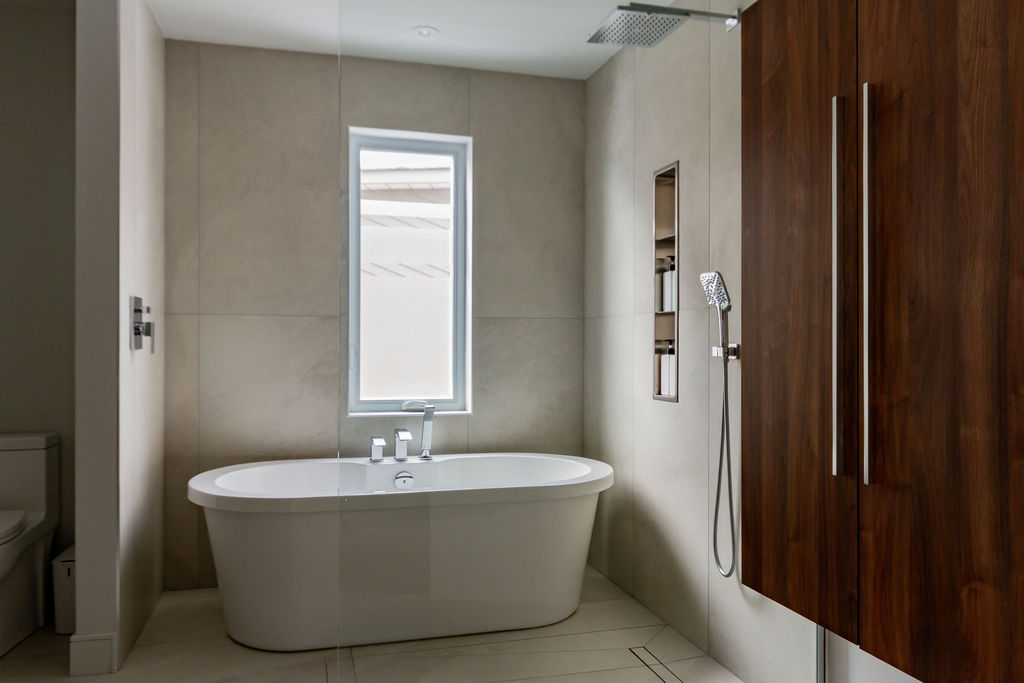 Salle de bain contemporaine à Montréal conçue par un designer d'intérieur, avec armoire de rangement en bois de noyer, baignoire autoportante sous la fenêtre et zone de douche italienne vitrée.