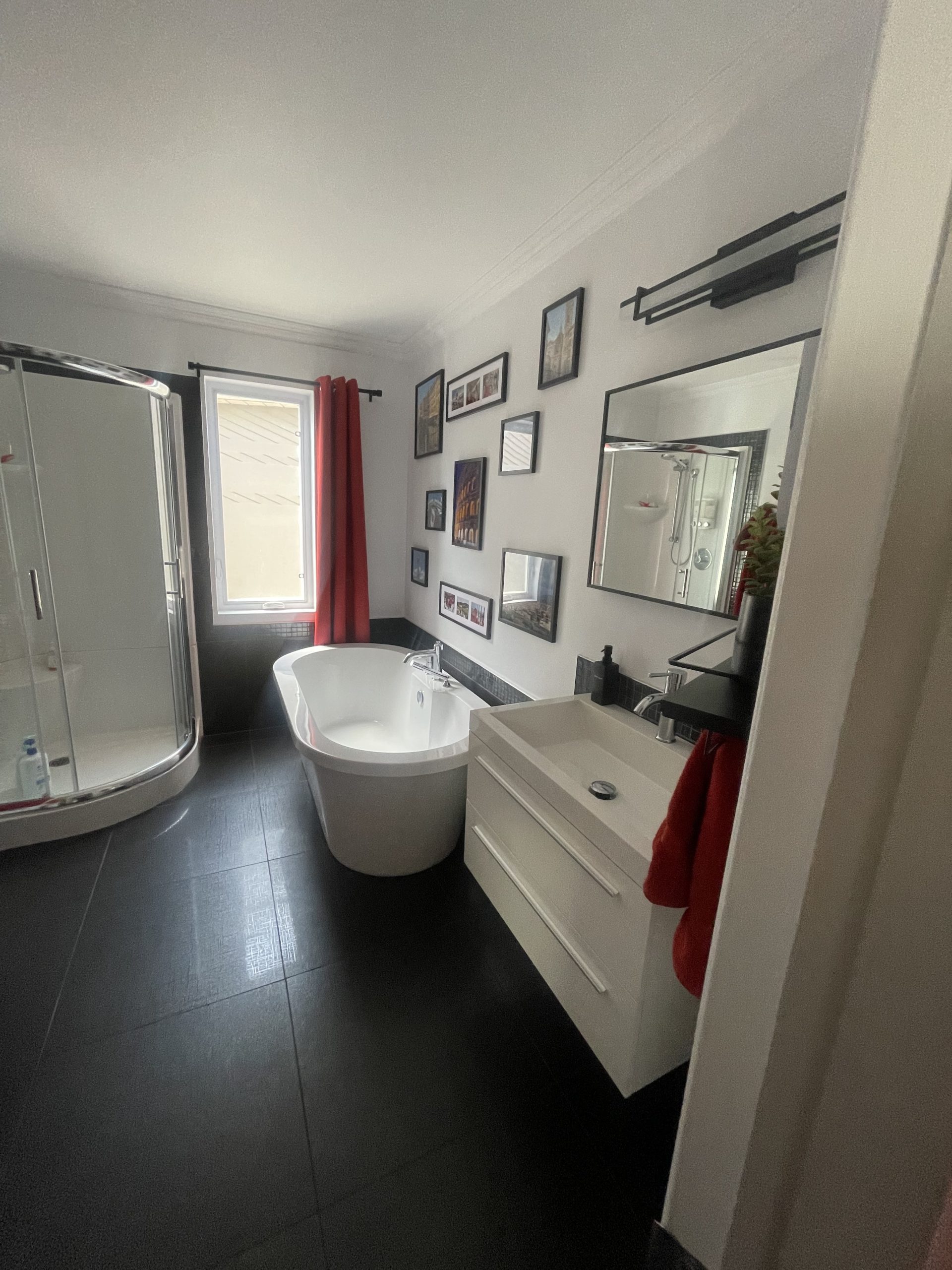 Salle de bain à Montréal AVANT les rénovations de design d'intérieur : ancienne cabine de douche en coin, murs blancs encombrés de cadres et rideaux rouges.