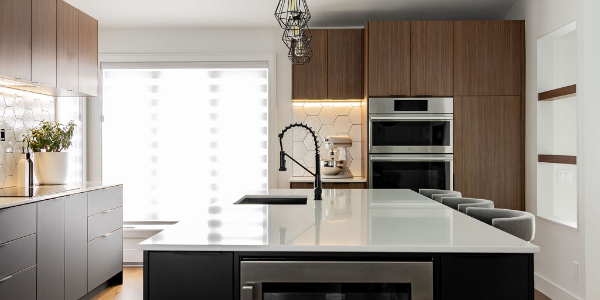 Vue globale d'une cuisine contemporaine à Montréal conçue par un designer d'intérieur, avec grand îlot noir, comptoir en quartz blanc,cellier encastré et armoires en bois chaleureux.
